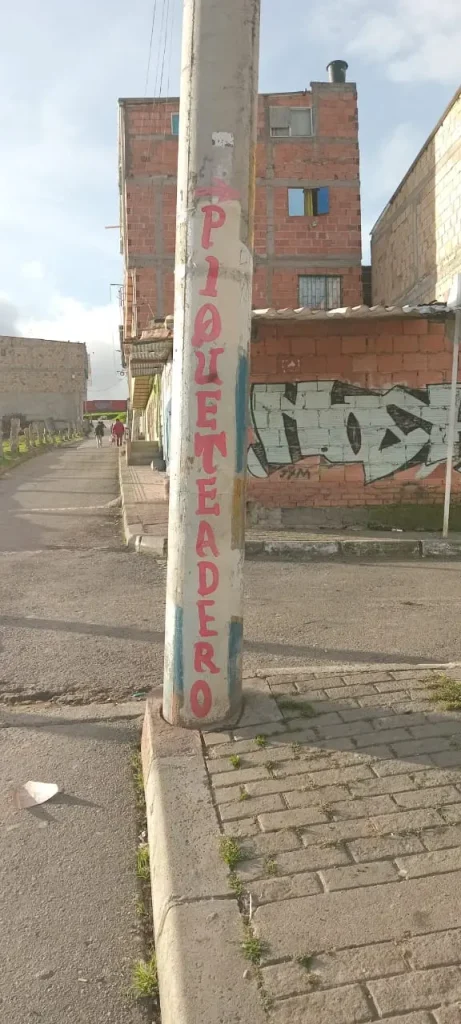 Mensaje pintado a mano en un poste de concreto en un barrio popular latinoamericano, reflejo de la creatividad urbana cotidiana en el reportaje Avisos Latinoamericanos.