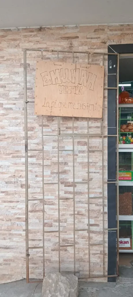 Aviso callejero artesanal de “Emuna Yeshua” colgado en una reja metálica, fotografiado para el reportaje gráfico “Avisos callejeros latinoamericanos, creatividad ilimitada” de El Pájaro Azul en la sección Encuadre