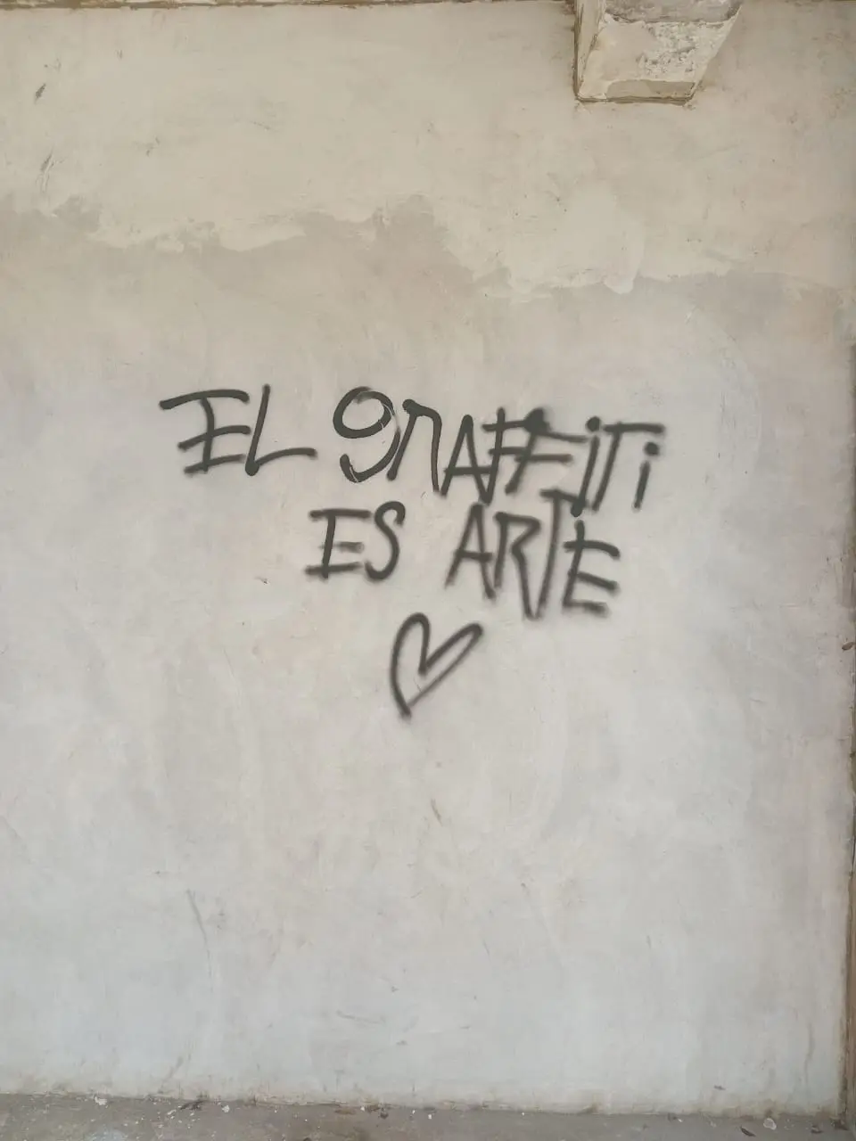 garffiti en tinta negra sobre pared blanca se ve parte de columna arriba a un lado y se lee el graffiti es arte, seccion encuadre del fotorreportaje avisos callejeros latinoamericanos. creatividad ilimitada de el pajaro azul medio digital de cronicas y reportajes